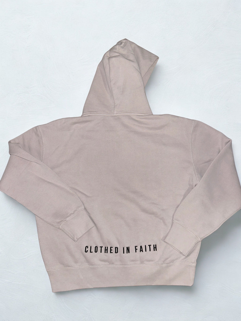 Beige hoodie with 'Clothed in Faith' text on a light gray background