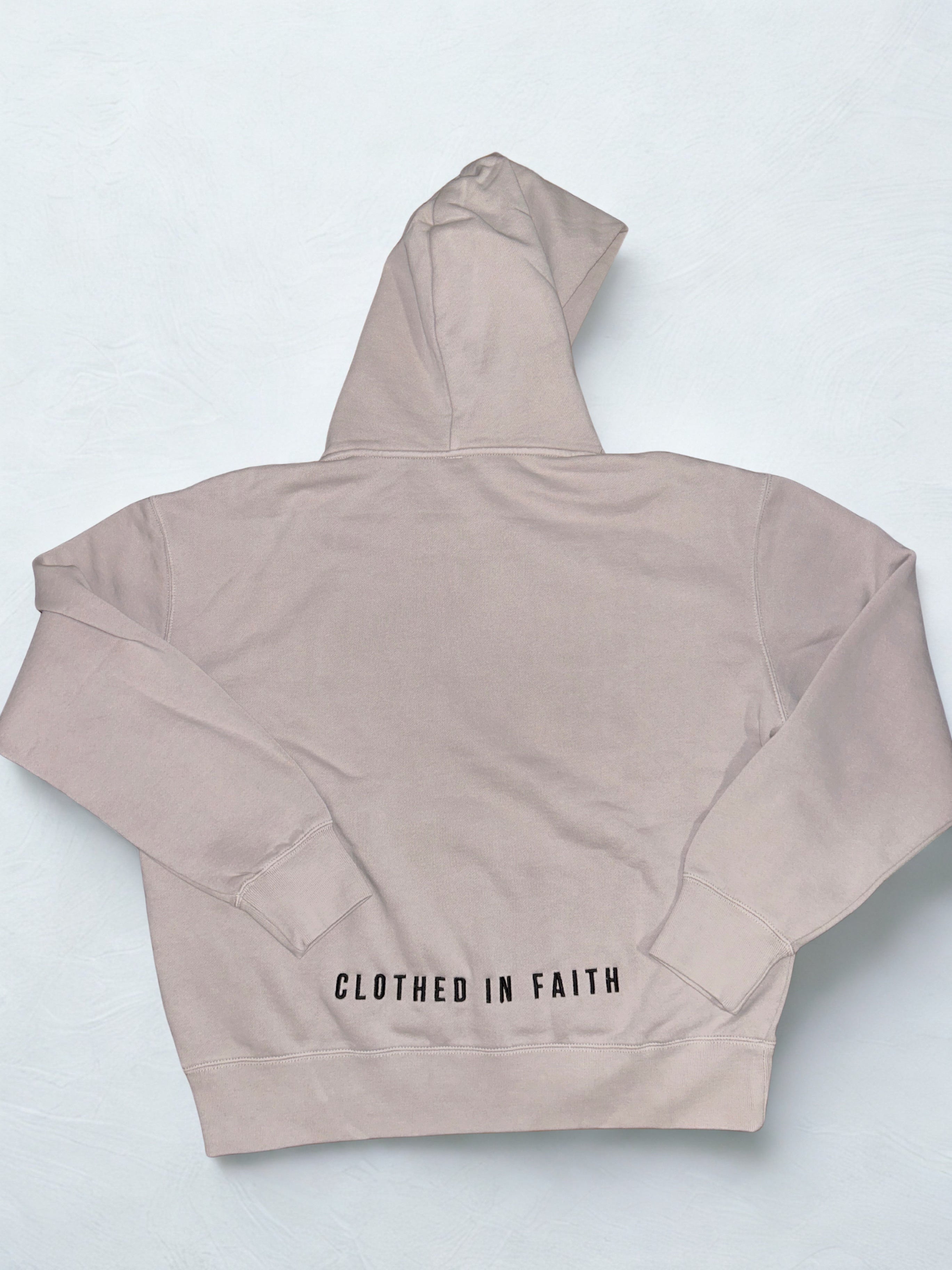 Beige hoodie with 'Clothed in Faith' text on a light gray background